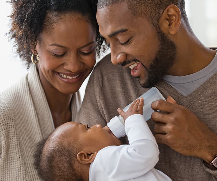 Mamá y papá felices alimentando a su bebé con un biberón