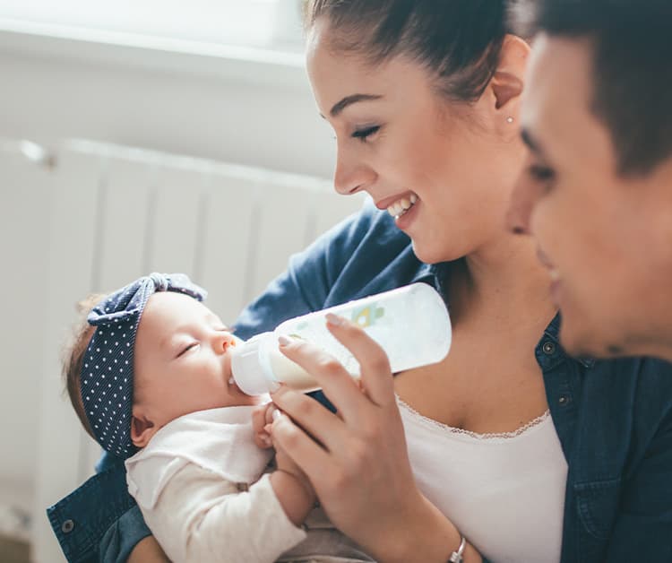 Madre alimentando a su bebé con biberón y su padre mirando sonriente