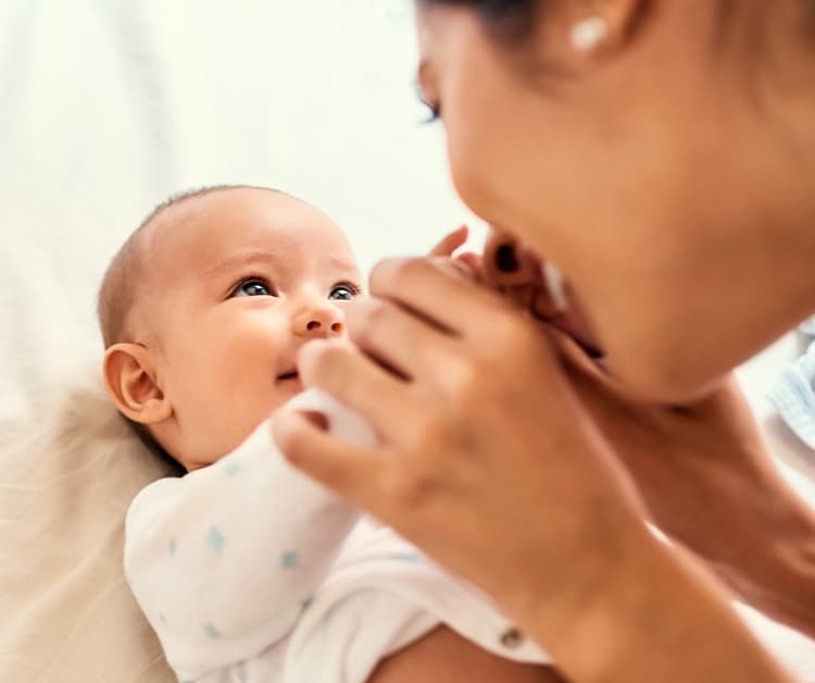 Bebé sonriente sostenido por mamá que agita un sonajero colorido